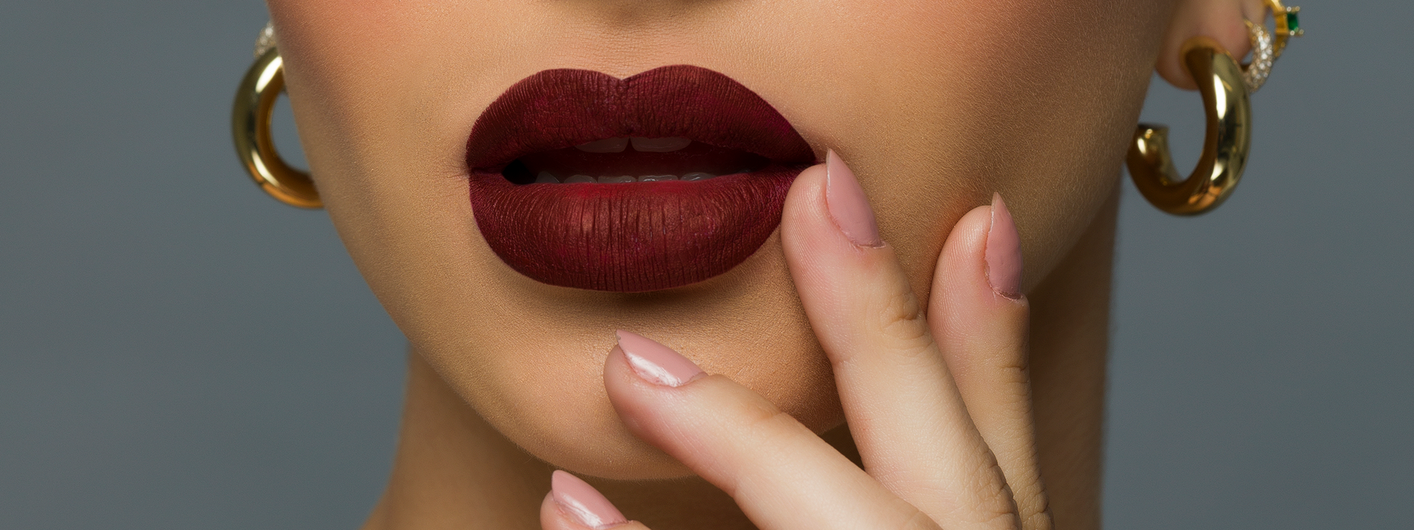 Close-up of a woman's face with red lipstick and gold earrings on a gray background
